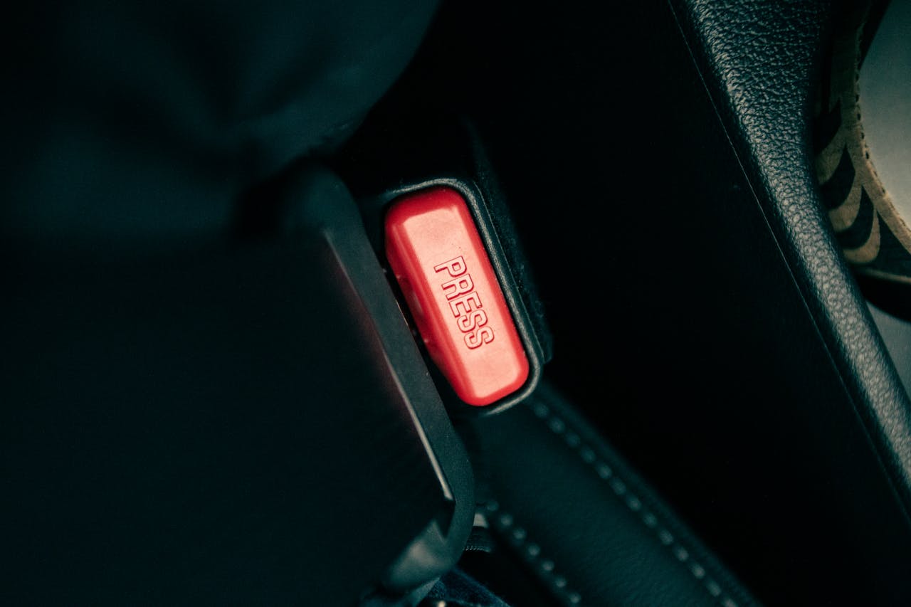 about-img-02 Detailed view of a car seatbelt buckle with a red press button.